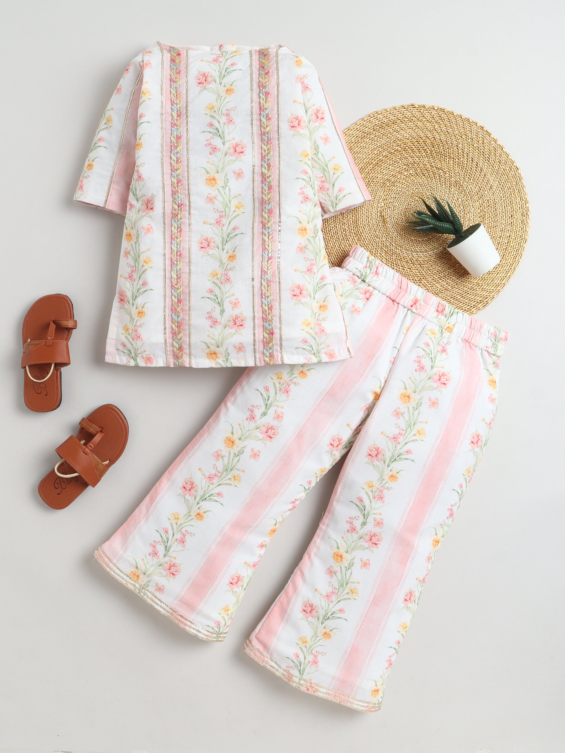 Floral outfit with pants and top, straw hat, and sandals on a light gray background