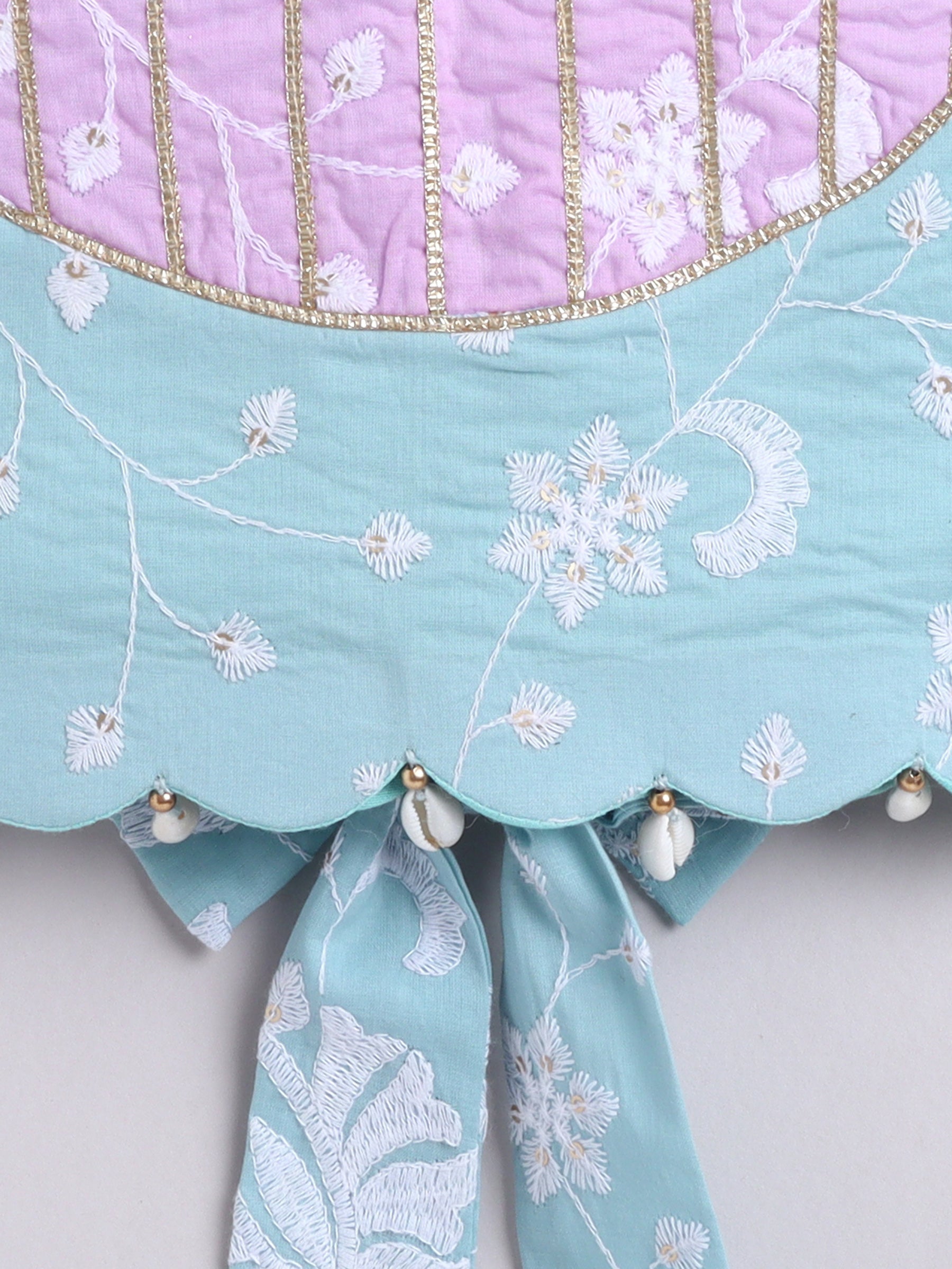 Close-up of a piece of fabric with floral embroidery and decorative elements on a light gray background.