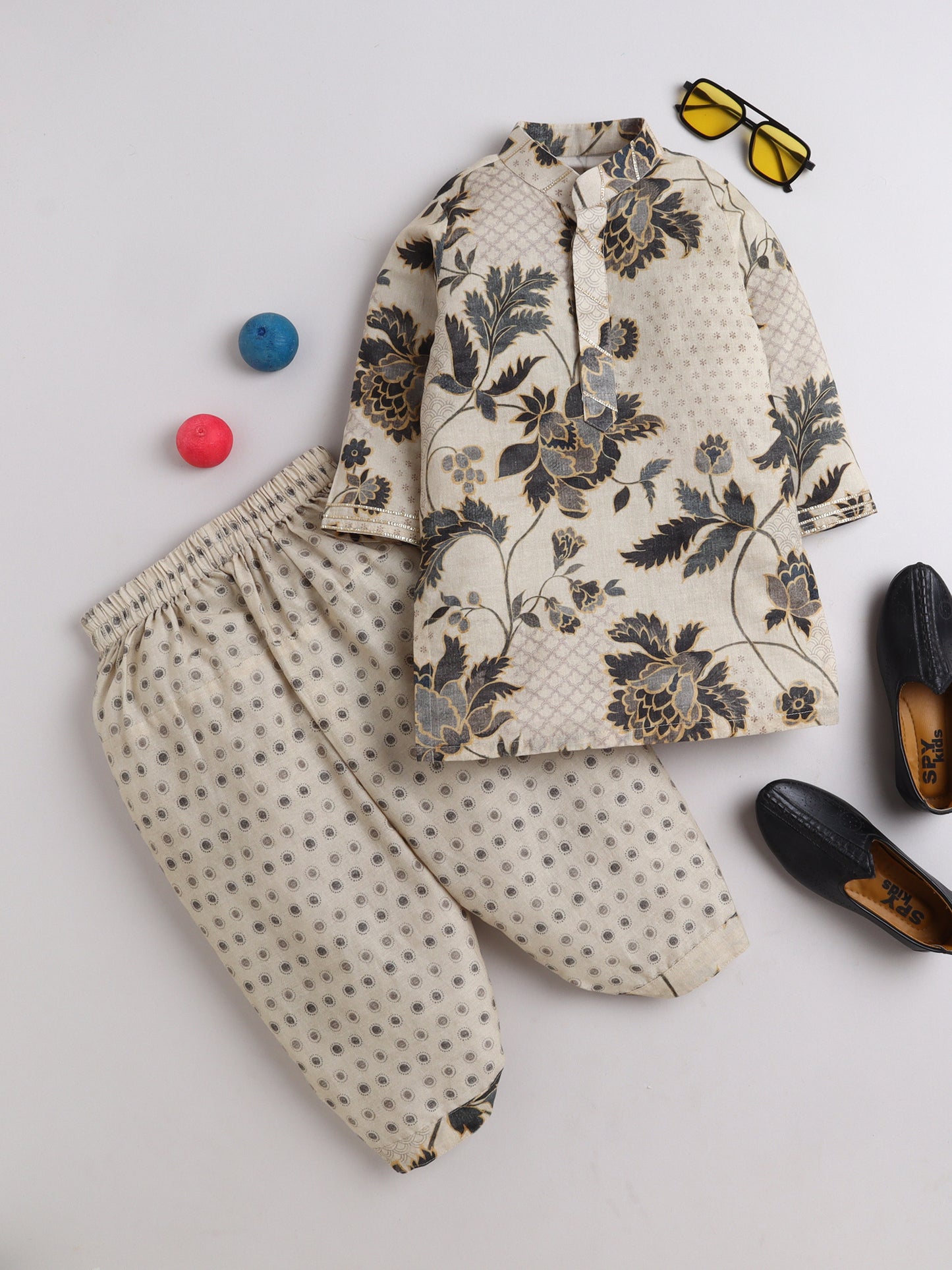 Beige cotton floral printed kurta and polka dot dhoti set for boys, displayed with accessories including black loafers, sunglasses, and colorful balls – traditional kidswear outfit from Fun Little Ones