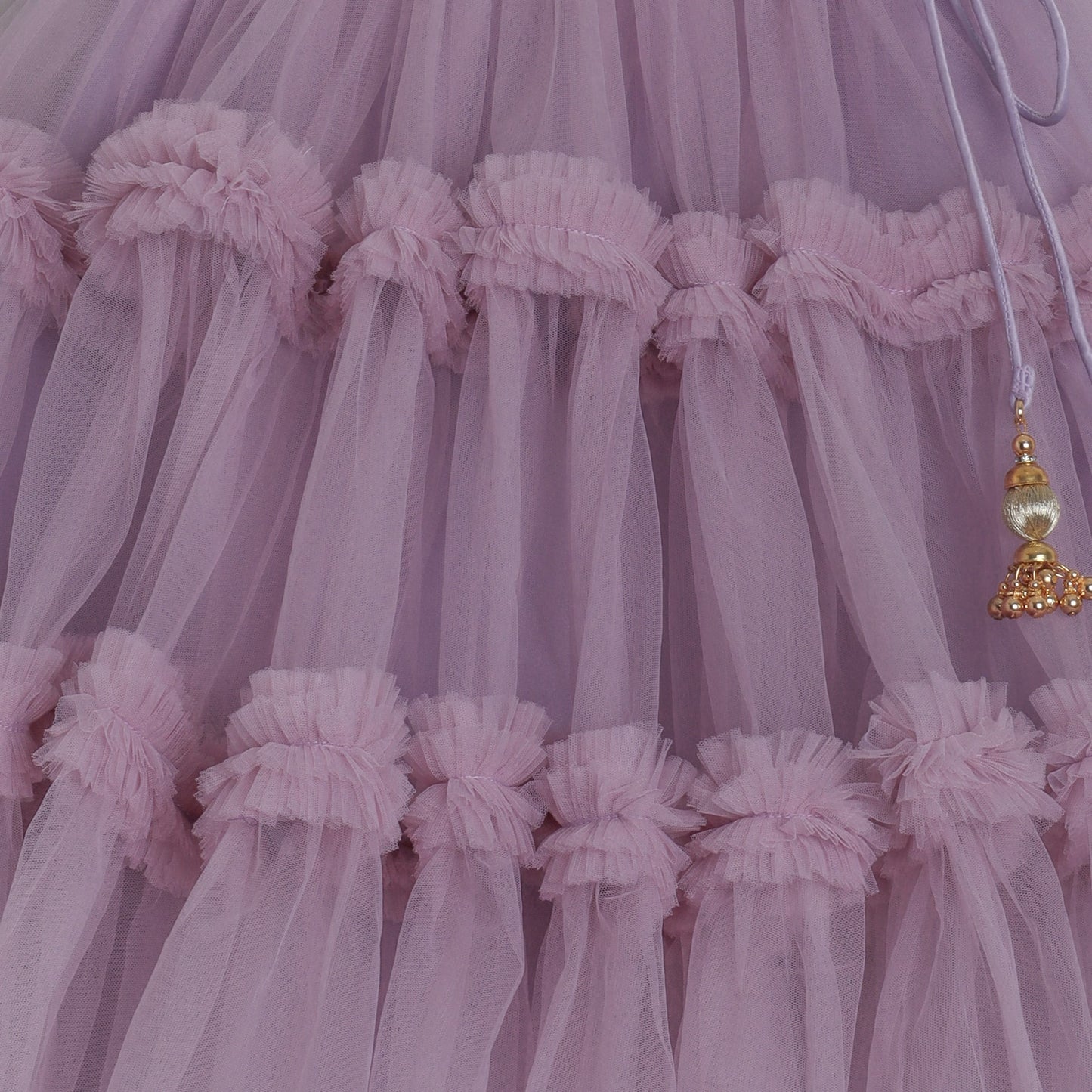 Close-up of a lilac tulle lehenga skirt with decorative gold tassel.