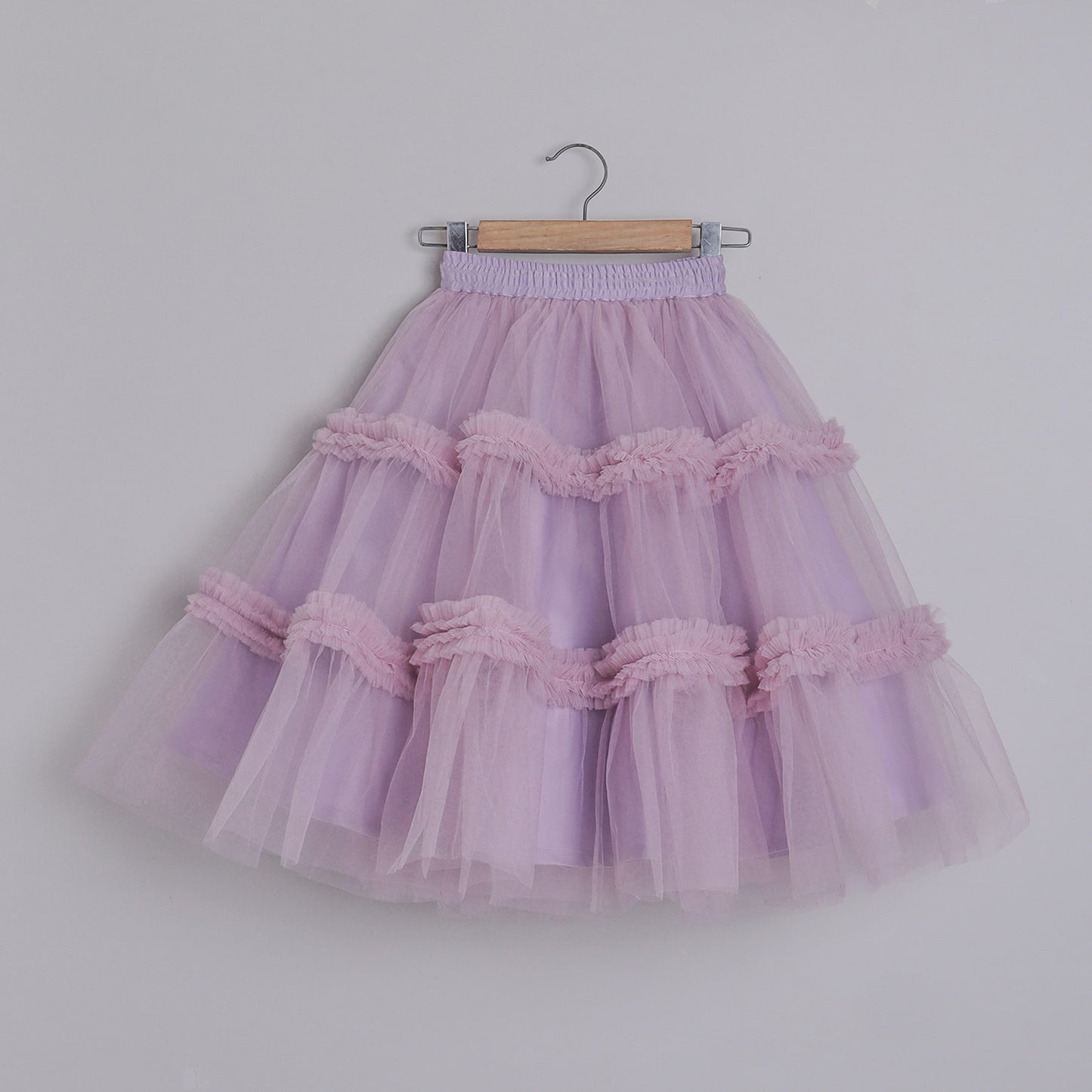 Lavender tulle skirt with ruffles on a wooden hanger against a plain background