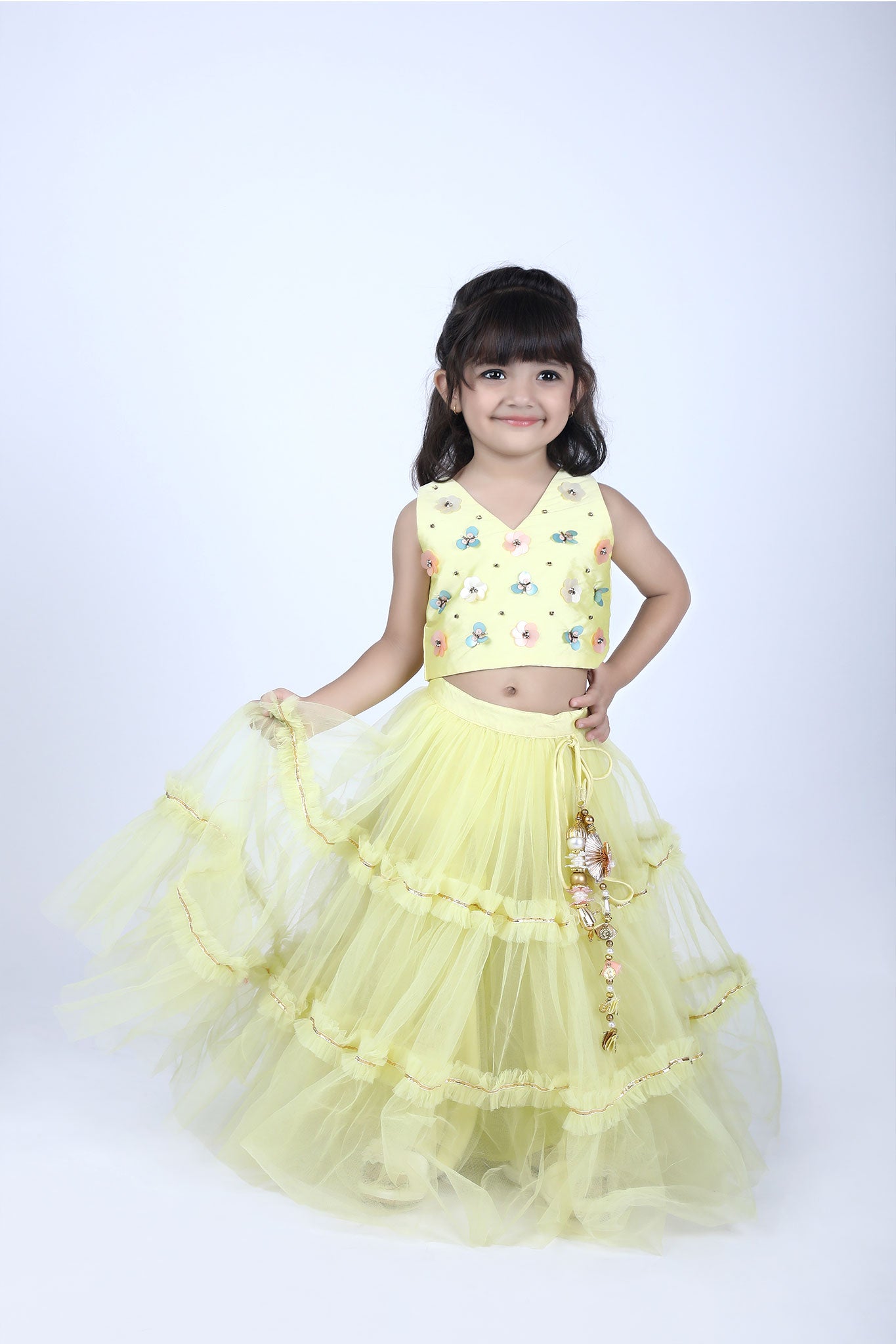 Front view of a girl wearing a sunshine yellow lehenga choli set with floral embroidered blouse and ruffled net skirt with tassels