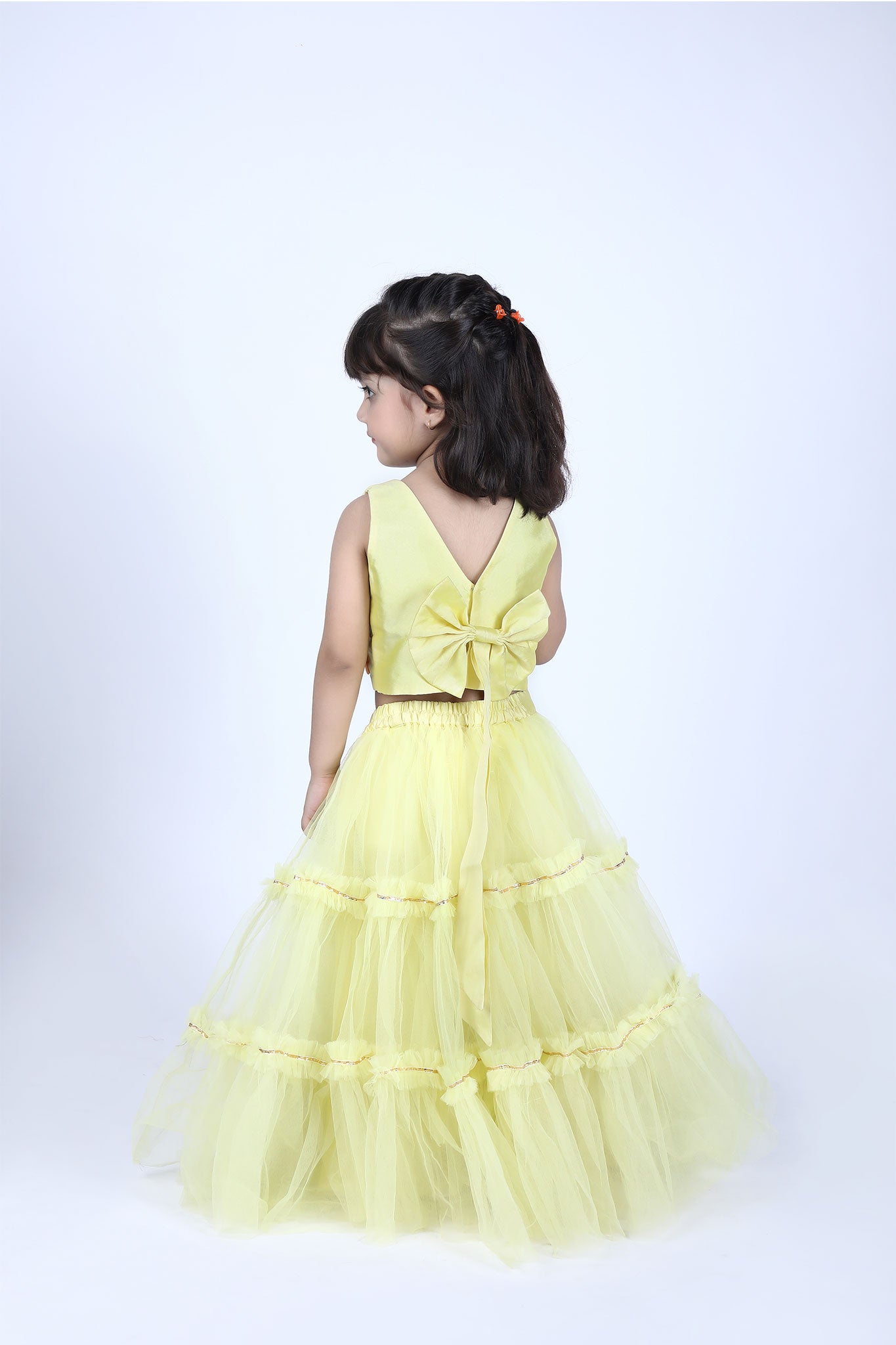 Back view of yellow lehenga choli set for girls featuring deep V-back with a bow blouse and flared skirt with soft net layers.